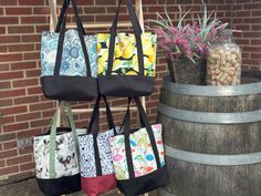 three bags are hanging on a rack next to a barrel with flowers and rocks in it