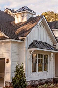 a white house with black shingles on the roof and two garages in front