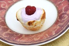 a small pastry with white icing and raspberry on top sits on a plate