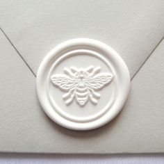 a white wax stamp with a bee on it's side and an envelope in the background