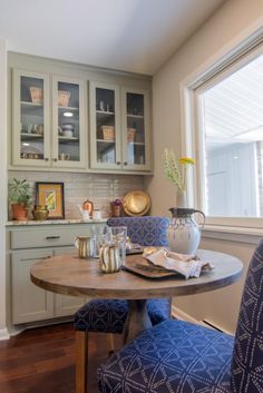 a dining room table with blue chairs in front of it and shelves on the wall