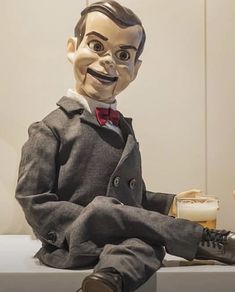 a creepy doll sitting on top of a counter next to a glass filled with liquid