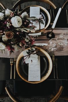 the table is set with black and gold place settings, silverware, and floral centerpieces