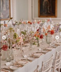 a long table with many vases filled with flowers and place settings on top of it