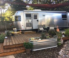 an airstream sits in the middle of a deck with chairs and plants on it