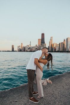 a man and woman kissing by the water in front of a large cityscape