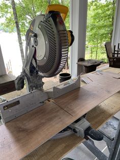 a table sawing machine on top of a piece of wood in a room with large windows