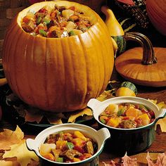 three bowls filled with stew sitting on top of a table next to pumpkins and autumn leaves