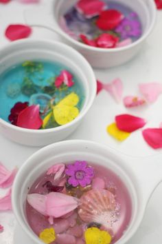 three white bowls filled with different types of flower petals and water in them, sitting on top of a table