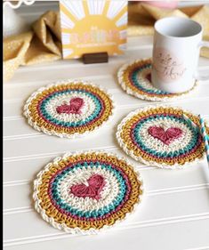 four crocheted coasters sitting on top of a table next to a cup