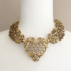 "Avon Jose and Maria Barrera necklace. Gold tone with rhinestones. This one has definite Victorian vibes with it's intricate scrolling. Adjustable length--at longest is around 14.5\". Can be adjusted to be more of a choker. Heavy. Signed Barrera on back. Does have some discoloration, but all stones are present. Please look closely at photos. Bib measurement of 2\" is the measurement of the heart. Thanks for visiting the shop! Make sure to stop back by!" Elegant Metal Rhinestone Necklace For Anniversary, Elegant Rhinestone Necklace For Anniversary, Vintage Gold Rhinestone Necklace With Sparkling Stones, Elegant Antique Gold Jeweled Jewelry, Antique Gold Jewelry With Rhinestones, Gold Vintage Rhinestone Necklace, Metal Rhinestone Necklace For Anniversary, Gold Crystal Necklace With Intricate Design, Gold Necklaces With Intricate Crystal Design