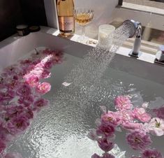 a bathtub filled with water and pink flowers next to a bottle of wine on a counter