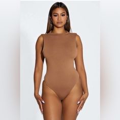 a woman in a tan bodysuit posing for the camera with her hands on her hips