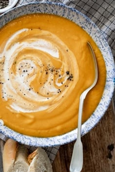 there is a bowl of soup on the table with bread and spoons next to it