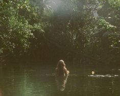 a woman swimming in the middle of a river surrounded by lush green trees and foliage