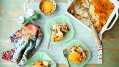 a table topped with green plates filled with food and serving utensils next to a casserole dish