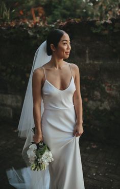 a woman in a white wedding dress holding a bouquet and looking off to the side