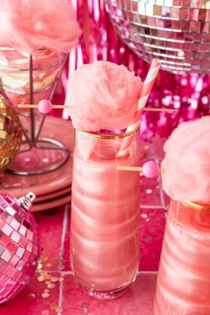 two pink cocktails with strawberries in them sitting on a table next to disco balls