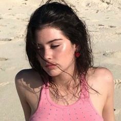 a young woman in a pink tank top on the beach with her eyes closed and hair blowing back