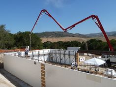 a crane is working on the roof of a building under construction in an area with hills and trees