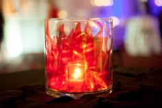 a lit candle is in a glass filled with water and red tissue paper streamers