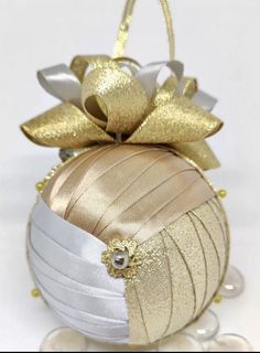 an ornament with gold and white ribbons on it's side, hanging from a string