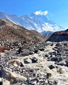 there is a man that is walking on the rocks in the water and mountains behind him