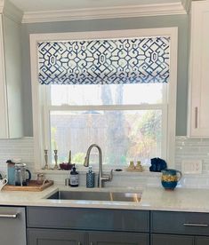 a kitchen with a sink, dishwasher and window covered in blue roman shades