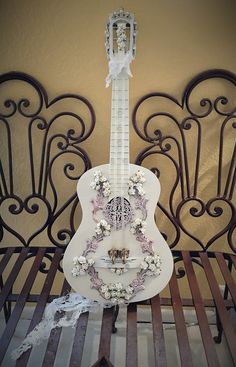 a white guitar sitting on top of a wooden bench next to a metal headboard