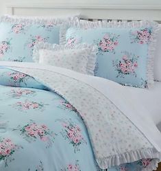 a blue bed with pink flowers and ruffles on the comforter is in front of a white headboard