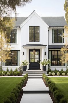 a large white house with black windows and plants in the front yard, along with steps leading up to it