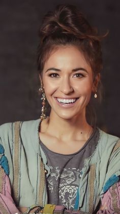 a smiling woman with her arms crossed in front of her chest and wearing earrings on top of her head