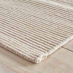 a close up view of a beige rug on a wooden floor, with the end of it