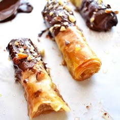 three chocolate covered pastry sticks sitting on top of a white countertop next to melted chocolate