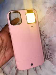 a hand holding a pink cell phone with a light on it's back side