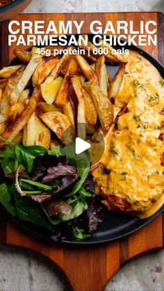 a black plate topped with chicken and french fries next to a salad on a wooden cutting board