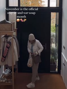 a woman standing in front of a black door holding a bag and looking at her cell phone