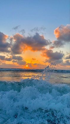 the sun is setting over the ocean with waves crashing in front of it and some clouds