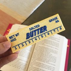 a person holding up a book with a butter label on it's side and an open book in the background