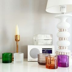 a white table topped with lots of different colored glass cups and vases next to a lamp