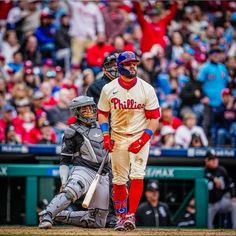 a baseball player holding a bat next to home plate with fans in the stands behind him