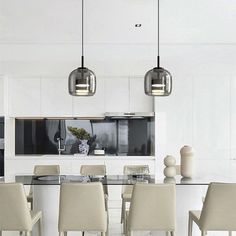 a dining room table with chairs and lights hanging from it's ceiling over the kitchen