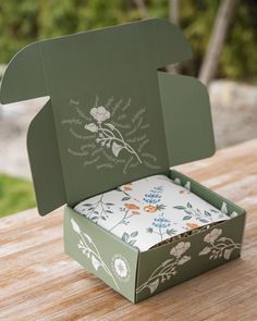 an open green box sitting on top of a wooden table next to a white napkin