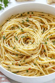 a white bowl filled with pasta and garnished with parsley on the side