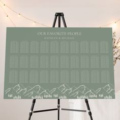 a green and white wedding seating chart on a easel with lights in the background