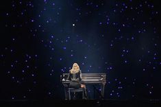 a woman sitting at a piano in front of a stage with blue lights on it