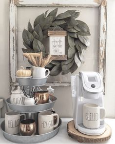 there is a coffee maker and mugs on the counter in front of a wreath