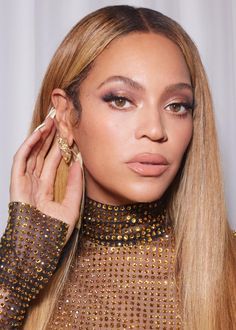 a woman with long blonde hair wearing a gold dress and holding a pair of earrings