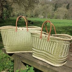 two large woven baskets sitting on top of a wooden bench next to a park filled with green grass