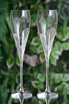 two wine glasses sitting next to each other in front of green plants and foliage on a sunny day